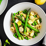 A vibrant, overhead shot of "Pasta Primavera One-Pot" dish. Focus on the fresh green asparagus, peas, and zucchini. Garnish with lemon zest and parsley. The setting is a bright, sunny kitchen.